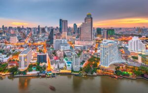 Vue panoramique de Bangkok au coucher du soleil, mettant en valeur ses gratte-ciels modernes, ses bâtiments emblématiques et le fleuve Chao Phraya traversant la ville