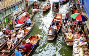 Scène animée d'un marché flottant en Thaïlande, avec des bateaux remplis de touristes et de marchandises colorées, naviguant sur un canal étroit bordé de stands locaux