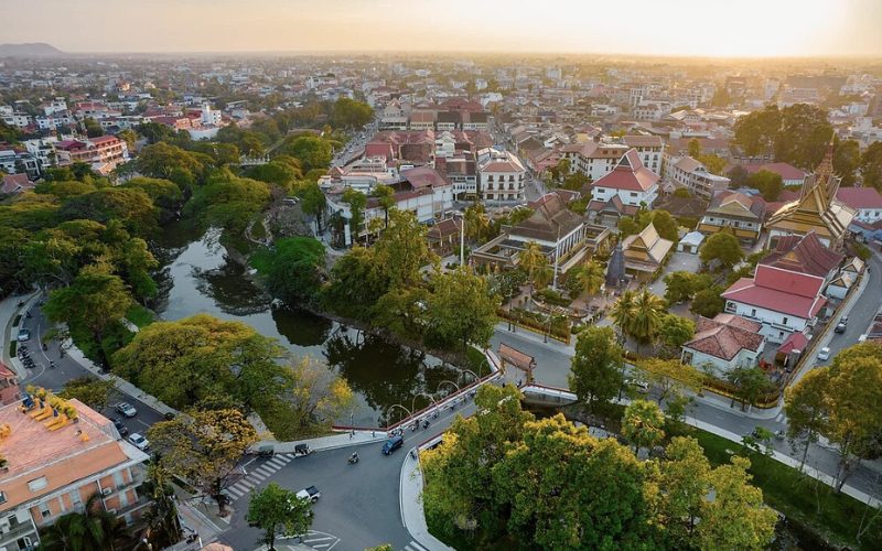 Vue aérienne de Siem Reap, au coucher du soleil, avec ses bâtiments traditionnels, ses espaces verts et un plan d'eau entouré de végétation